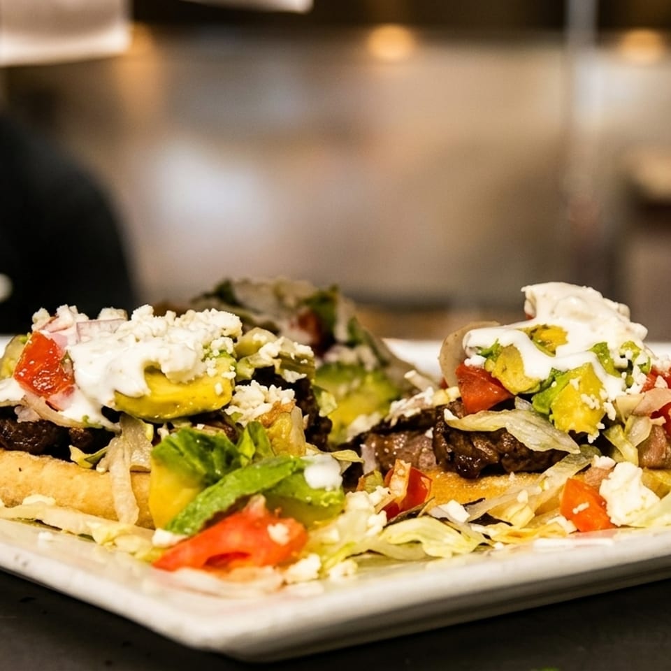 Two loaded sopes with meat, lettuce, avocado, tomatoes, sour cream, and cheese on a white plate.